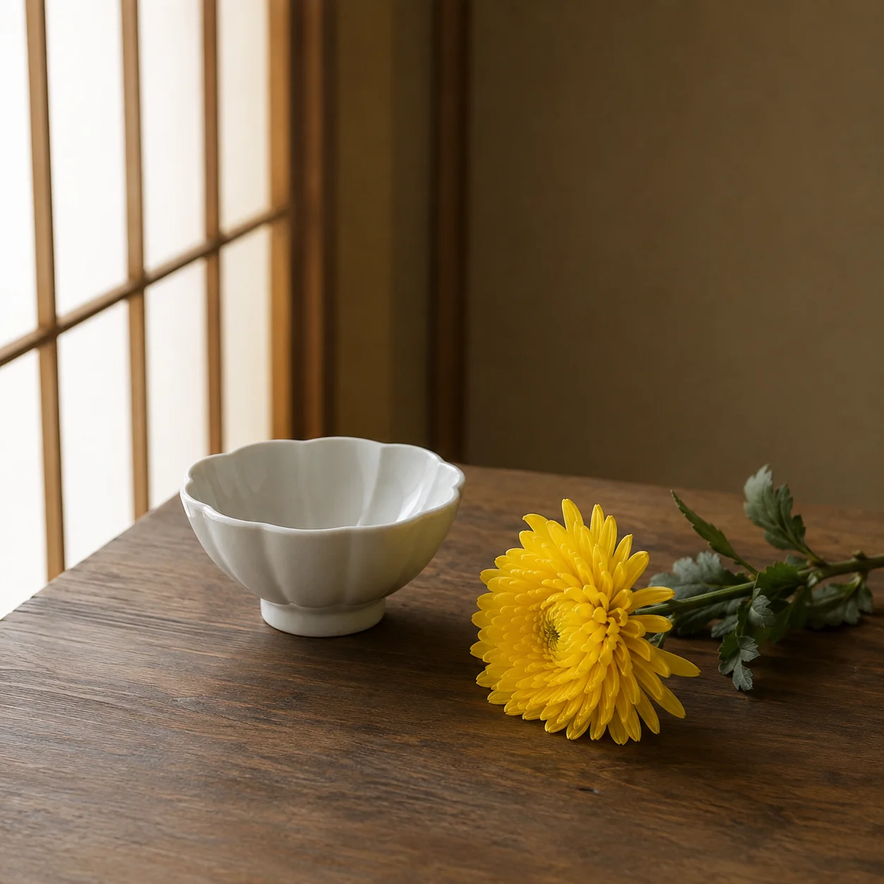 障子のそばの木のテーブルに、菊の花びらの形をした白い小鉢と、葉のついた黄色い菊が一輪横たえてある